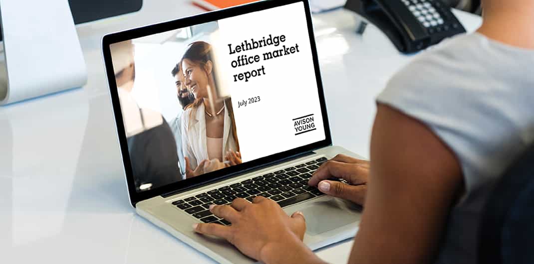 photo of a laptop on a table with a person's hands on the keyboard, the screen displays Avison Young's Lethbridge office market report July 2023